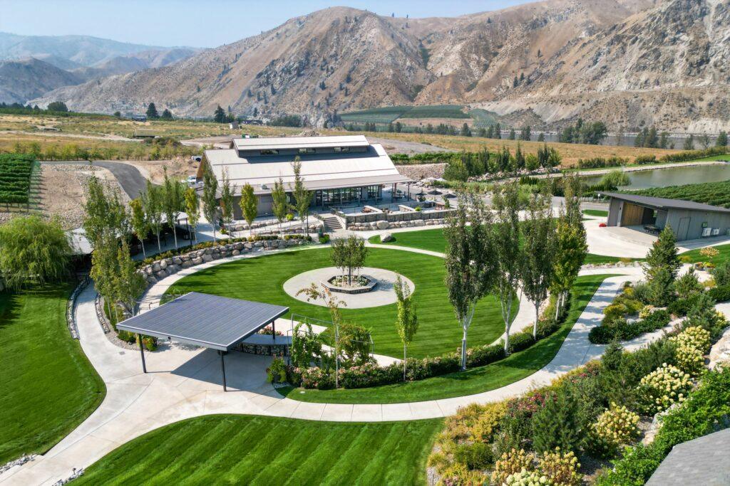 A landscaped garden with a circular lawn, surrounding pathways, a pavilion, and buildings nestled in a mountainous area.