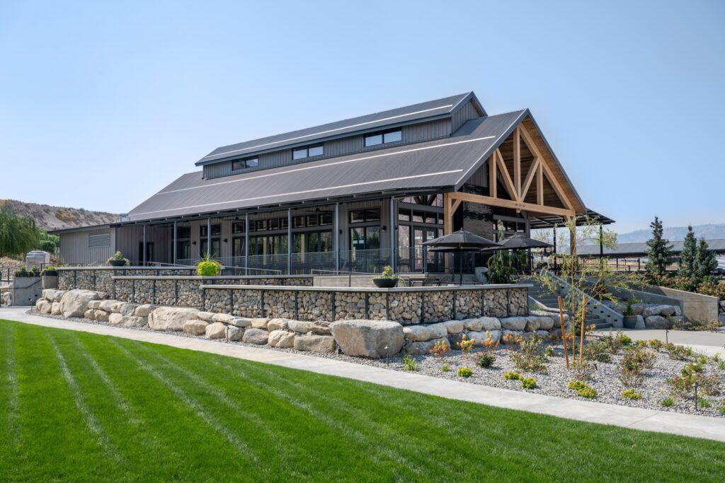 Large modern barn with metal roofing and large windows, surrounded by a well-kept lawn and stone landscaping.